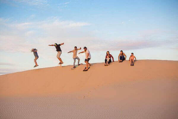 Adventurer enjoying sandboarding in Marrakech's Agadir sand dunes, with breathtaking desert views.